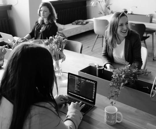 three people sitting around a desk, two working, one laughing at something off screen